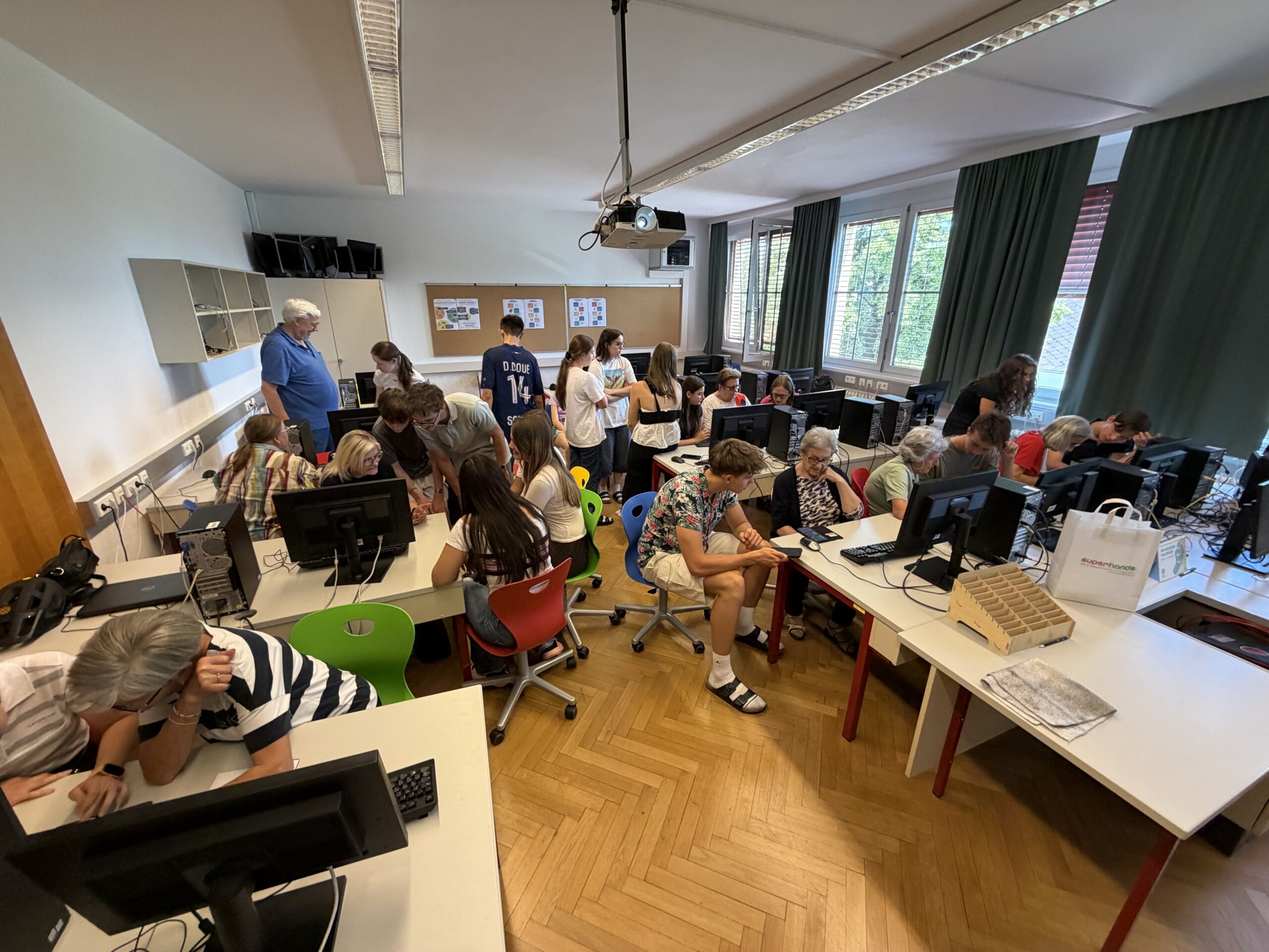 Begegnungen2 Ein Bild mit dutzenden alten und jungen Menschen wie sie zusammen im IT-Saal des ZBG arbeiten